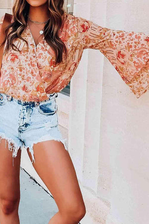 a woman wearing a floral blouse and denim shorts