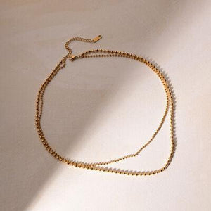 a necklace with a gold ball chain on a white surface