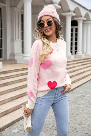 a woman wearing a pink heart sweater and jeans