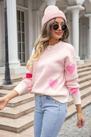 a woman wearing a pink heart sweater and jeans