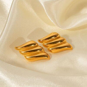 a pair of gold earrings sitting on top of a white cloth