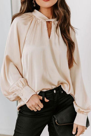 a woman wearing a beige blouse and black pants