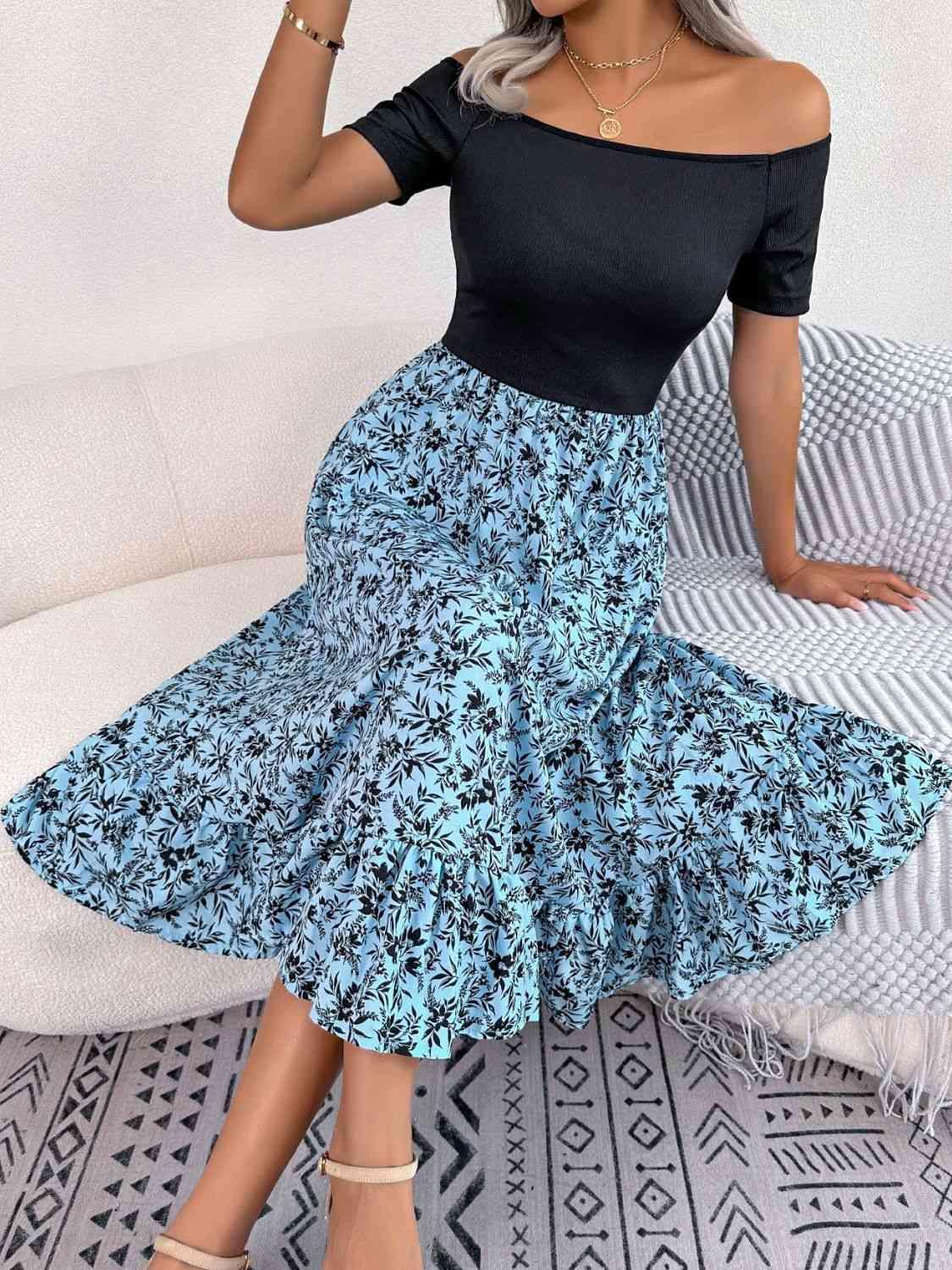 a woman sitting on a couch wearing a black top and blue floral skirt