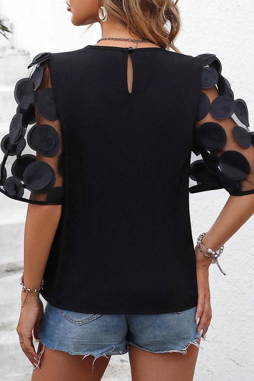 a woman wearing a black top with sheer sleeves