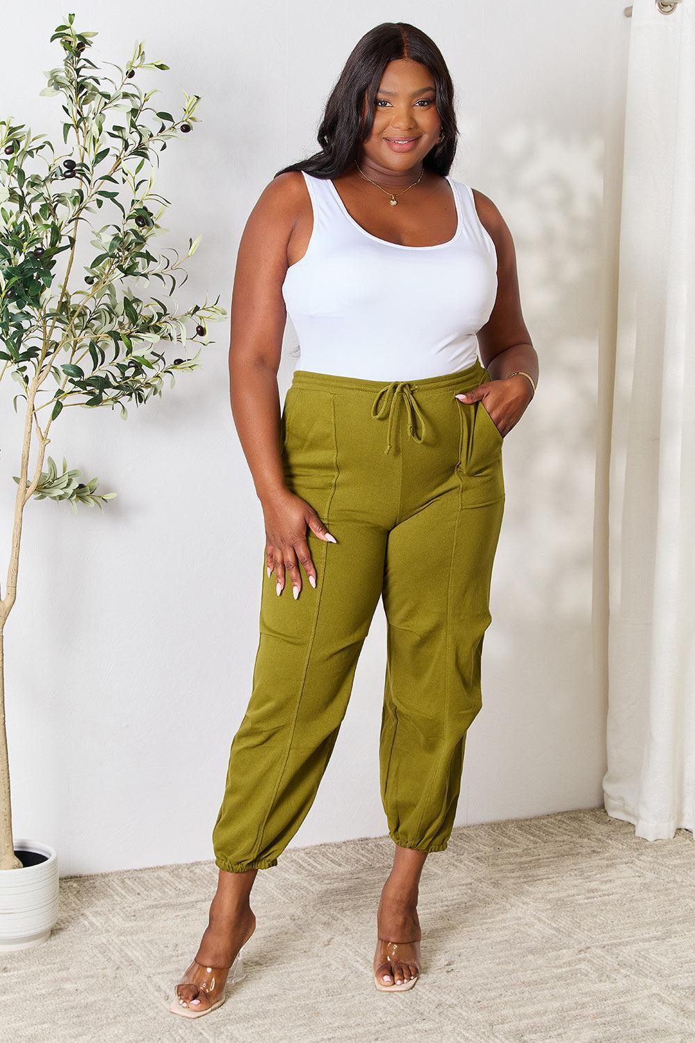a woman in a white tank top and green pants
