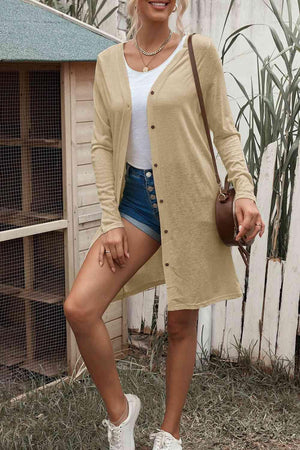 a woman standing in front of a fence wearing a tan cardigan