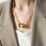 a woman wearing a gold chain necklace with a turquoise bead