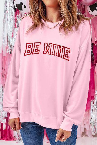 a woman wearing a pink sweatshirt that says be mine