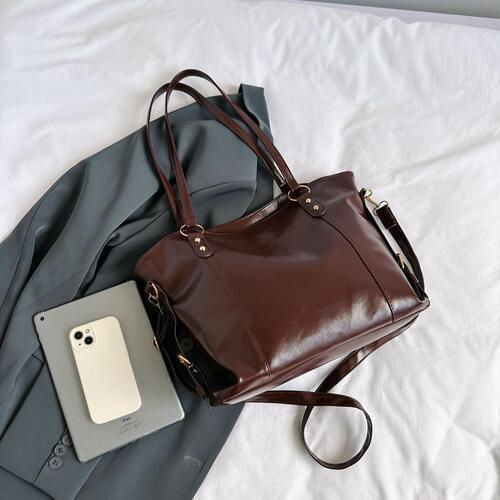 a brown purse sitting on top of a bed next to a cell phone