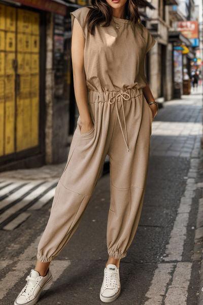 a woman standing on a street wearing a tan jumpsuit