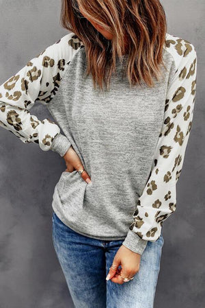 a woman wearing a grey and white top with leopard print sleeves