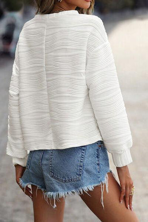 a woman wearing a white sweater and denim shorts