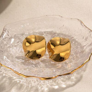 a pair of gold earrings sitting on top of a glass plate