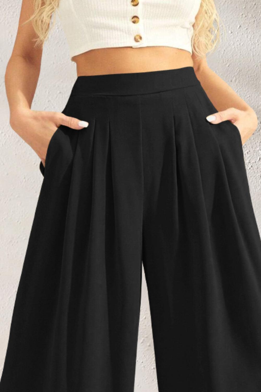 a woman wearing a white crop top and black wide legged pants