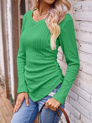 a woman leaning against a brick wall wearing a green sweater