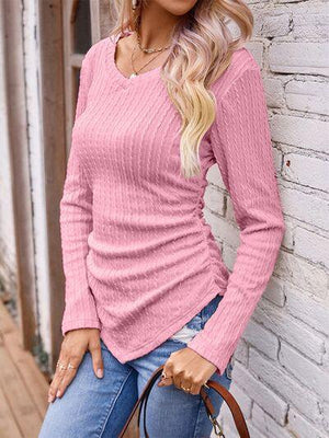 a woman leaning against a brick wall wearing a pink sweater and jeans