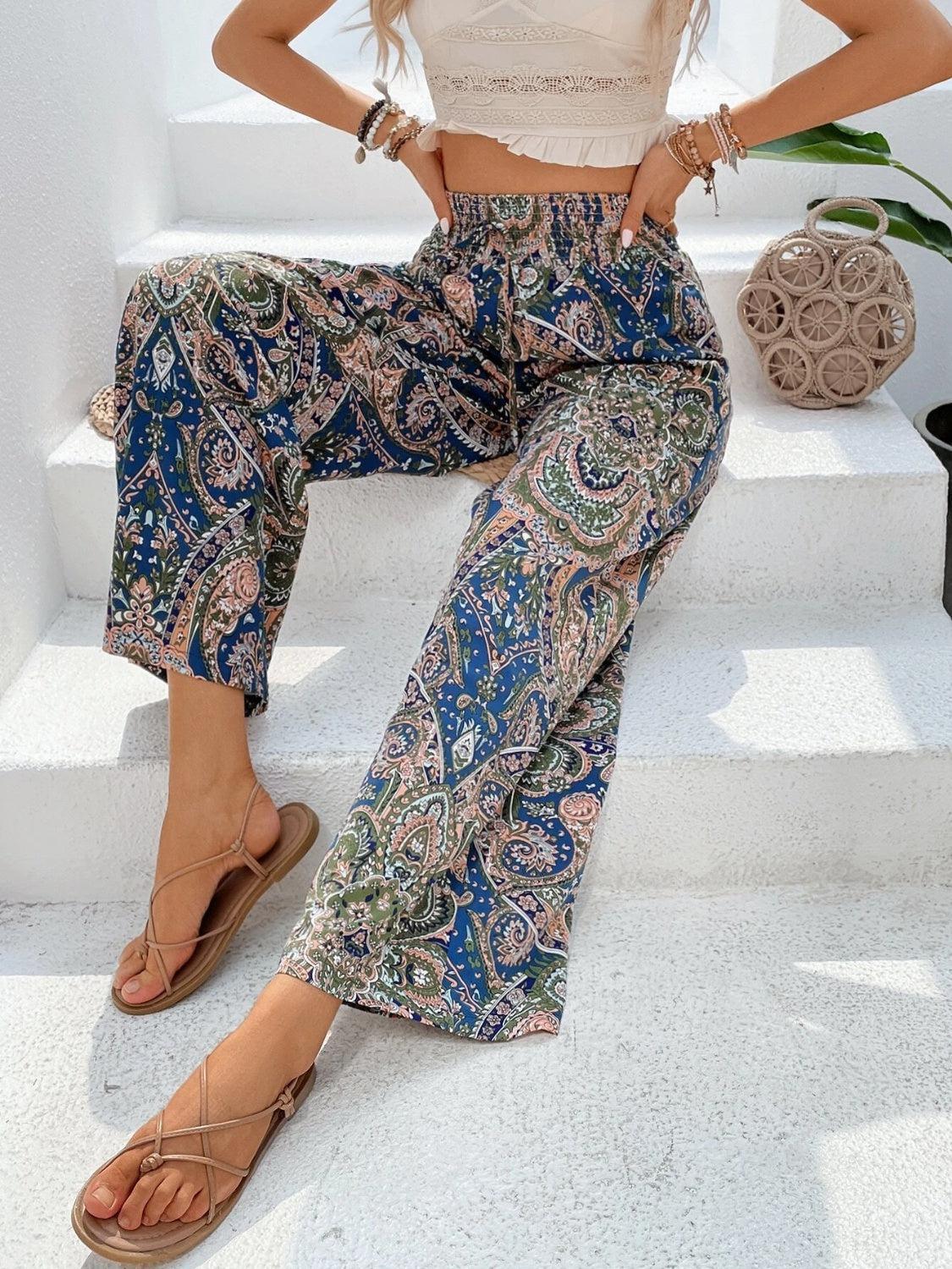 a woman sitting on a step wearing a white top and paisley print pants