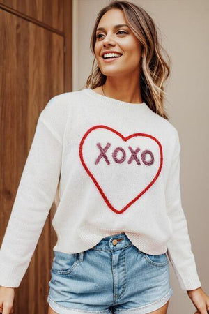 a woman wearing a white sweater with a heart on it