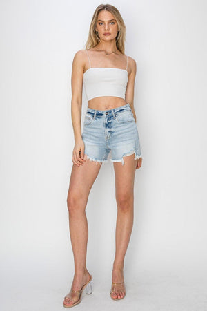 a woman wearing a white crop top and denim shorts