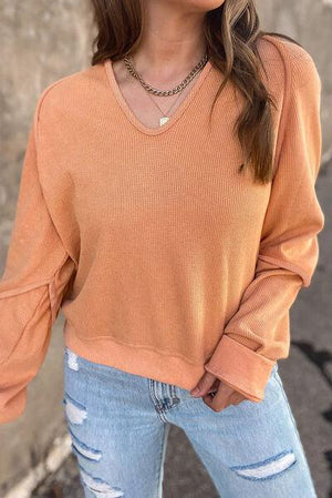 a woman wearing an orange sweater and ripped jeans