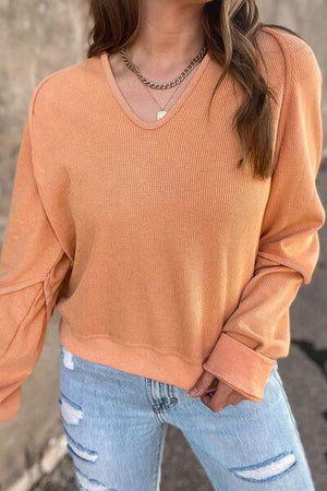 a woman wearing an orange sweater and ripped jeans