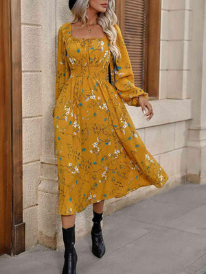 a woman in a yellow floral dress leaning against a wall