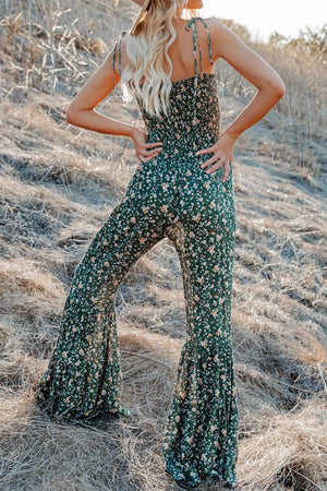 a woman standing in a field wearing a green floral jumpsuit