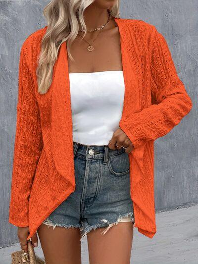 a woman wearing an orange cardigan sweater and denim shorts