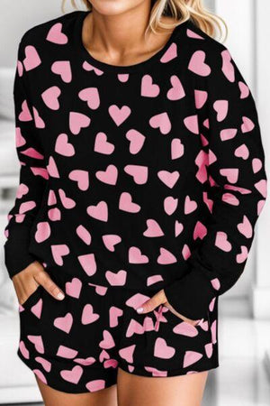 a woman wearing a black and pink heart sweater and shorts