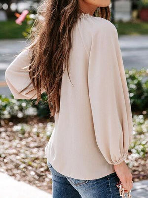 a woman with long hair wearing a tan blouse and jeans