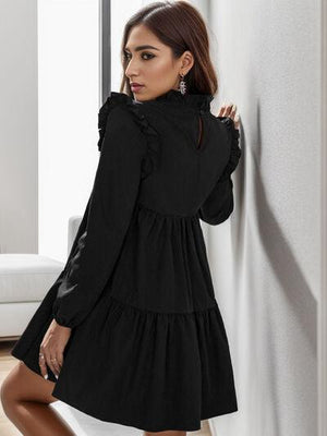 a woman in a black dress leaning against a wall