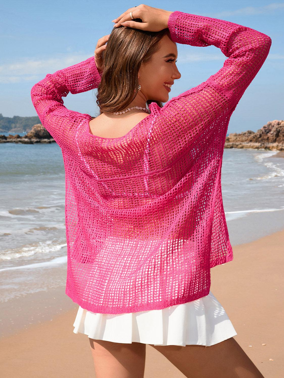 a woman standing on a beach wearing a pink sweater