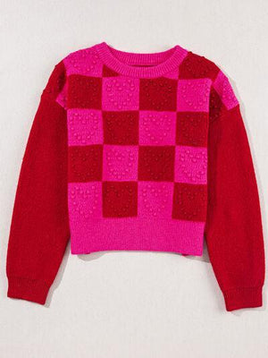 a pink and red sweater hanging on a wall