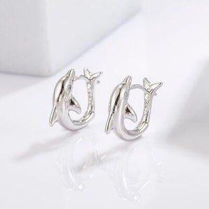 a pair of dolphin earrings sitting on top of a white surface