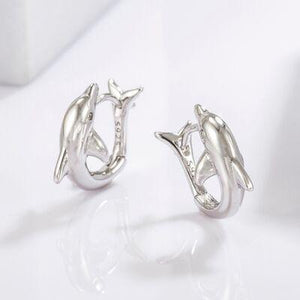 a pair of dolphin earrings sitting on top of a white surface