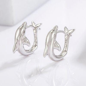 a pair of dolphin earrings sitting on top of a table