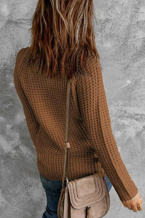 a woman in a brown sweater carrying a beige purse