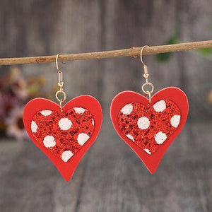 a pair of red heart shaped earrings hanging from a branch