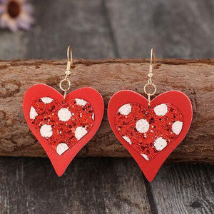 a pair of red heart shaped earrings sitting on top of a piece of wood