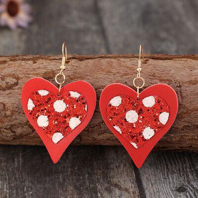 a pair of red heart shaped earrings sitting on top of a piece of wood