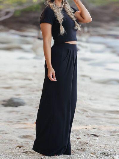 a woman standing on a beach wearing a black dress