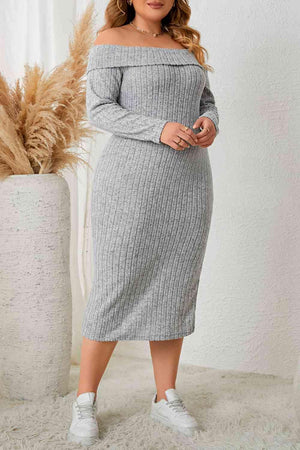 a woman in a grey sweater dress standing next to a plant