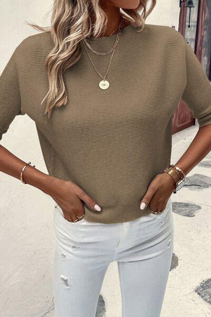 a woman wearing a tan sweater and white jeans