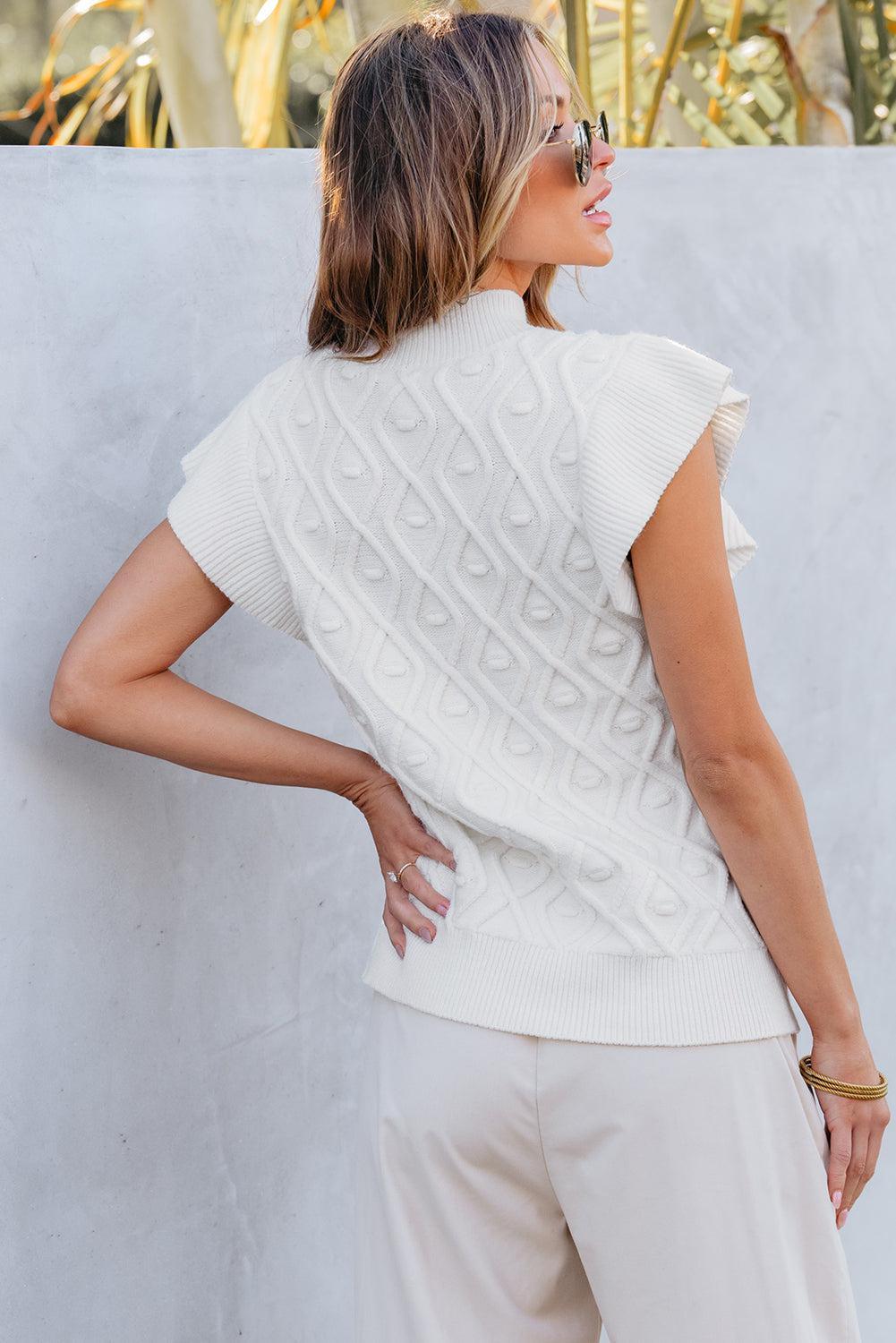 a woman in a white sweater leaning against a wall