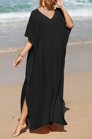 a woman in a black dress walking on the beach