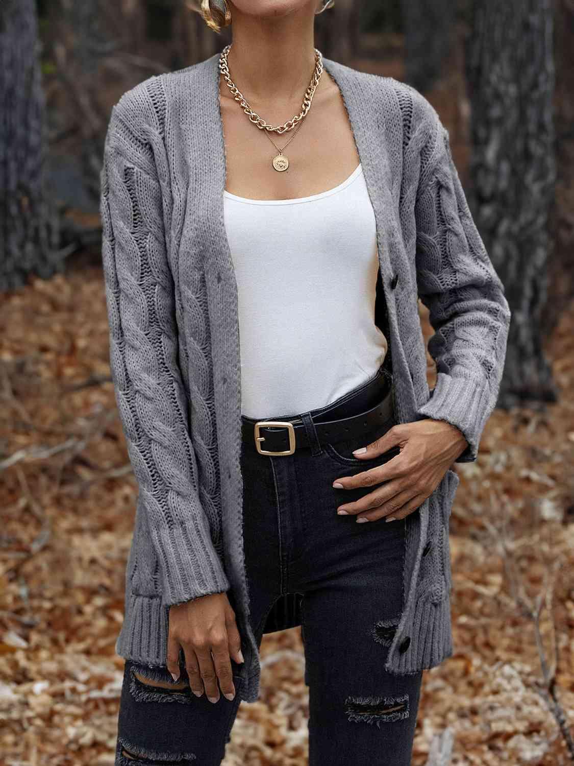 a woman standing in the woods wearing a gray cardigan