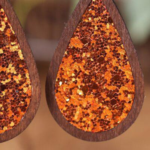 a pair of wooden earrings with orange and gold sequins