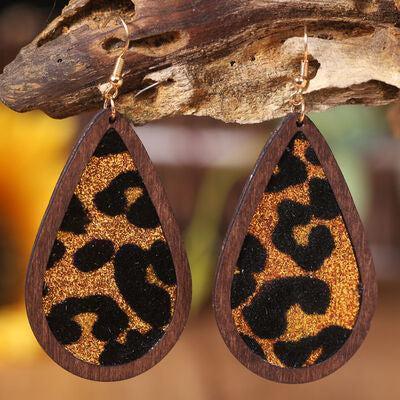 a pair of leopard print wooden earrings hanging from a tree branch