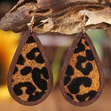 a pair of leopard print wooden earrings hanging from a tree branch