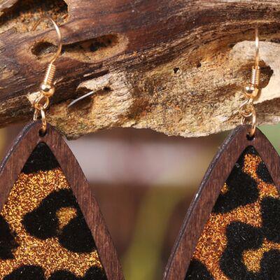 a pair of leopard print wooden earrings hanging from a tree branch